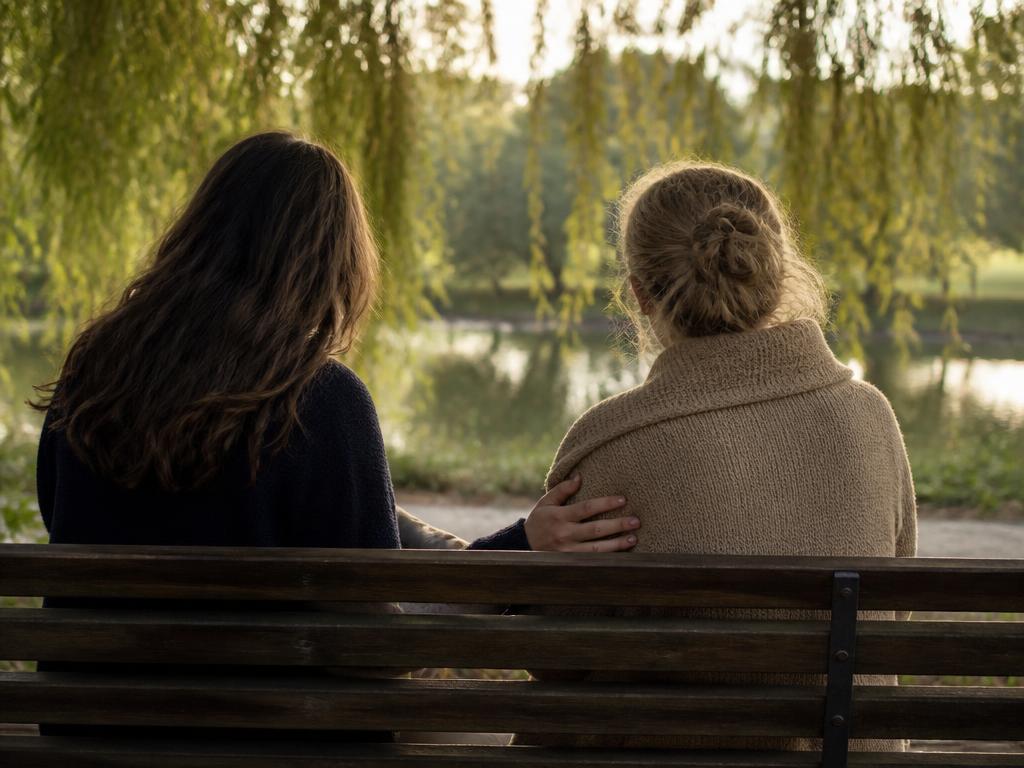 Two women sitting together on a bench beneath a willow tree